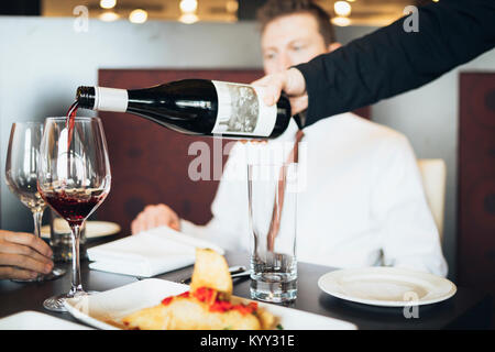 7/8 Hand der Kellner gießen Wein im Glas für Geschäftsreisende im Hotel Stockfoto