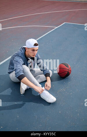 Hohe Betrachtungswinkel von Teenage boy Schnürsenkel binden während der Sitzung am Basketballplatz Stockfoto