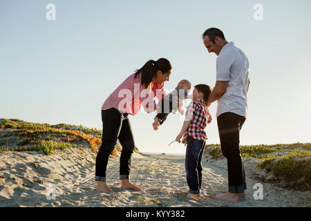 Baby Boy berühren Bruder, während die Mutter gegen den klaren Himmel am Strand durchgeführt werden Stockfoto