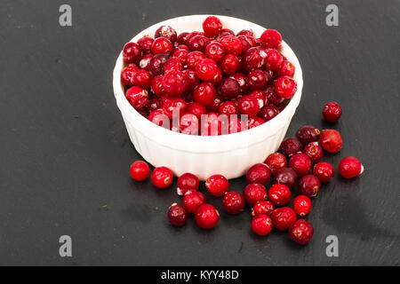 Gefrorene Beeren der Cranberries in Weiß Schüssel auf schwarzem Stein. Studio Foto Stockfoto