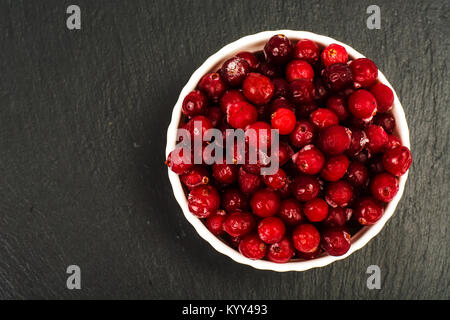 Gefrorene Beeren der Cranberries in Weiß Schüssel auf schwarzem Stein. Studio Foto Stockfoto