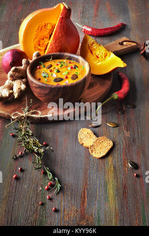 Würzige Kürbissuppe in Houten auf dunklem Hintergrund, serviert mit Kürbiskernen und Thymian. Bestandteile sind rund um die Schüssel. Stockfoto