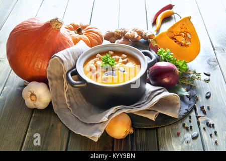 Pikante Kürbis creme Suppe mit Ingwer, Zwiebeln, Knoblauch und Chili in Keramik Schüssel auf den Holztisch. Die Suppe mit Croutons, Kürbiskerne serviert und Stockfoto