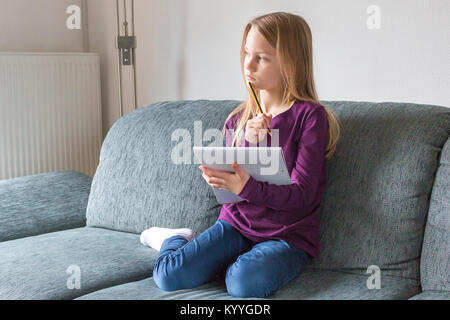 Ein Mädchen sitzt auf dem Sofa und denkt mit Stift und Notizblock in der Hand Stockfoto