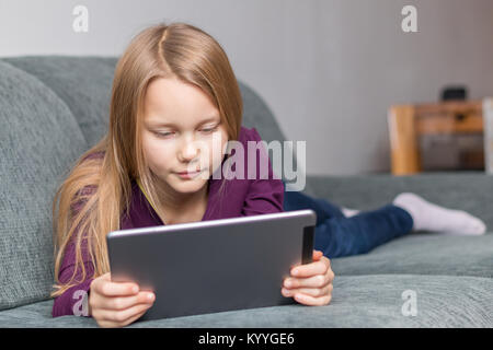 Ein Mädchen liegt auf dem Sofa mit einem Tablet-PC im Wohnzimmer Stockfoto