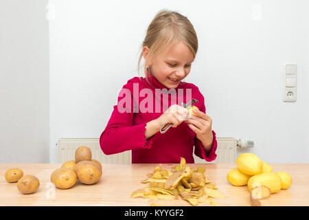 Ein Mädchen trägt ein rot rollkragen pullover. Er genießt, Schälen von Kartoffeln mit einem Schäler und lacht. Stockfoto