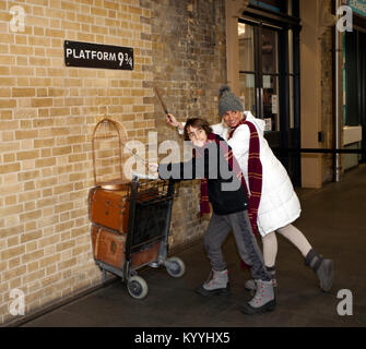 Harry Potter Fans pose mit Zauberstäbe und Gryffindor Schals durch eine Replik der Katze in Plattform 9 3/4 im Bahnhof Kings Cross, London Stockfoto