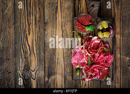 Antipasto catering Plattenteller mit Speck, ruckartig, Wurst und Oliven auf einer hölzernen Hintergrund. Ansicht von oben Stockfoto