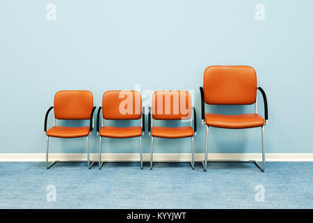 Eine große und drei kleine Stühle in einer Reihe gegen eine Wand in einem leeren Raum - Konzept Bild Stockfoto