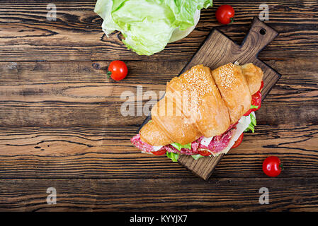 Leckeres Frühstück. Appetitlich Croissant mit Salami und Käse und Tomaten. Flach. Ansicht von oben Stockfoto