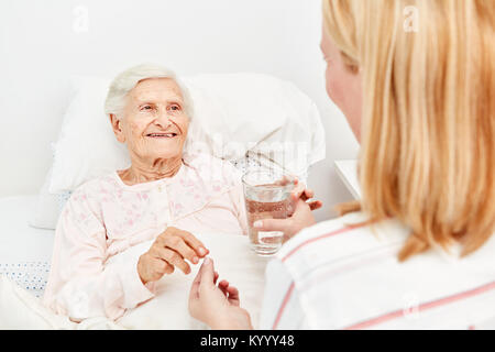 Kranke ältere Frau liegt im Bett und nimmt ein Medikament mit Wasser Stockfoto