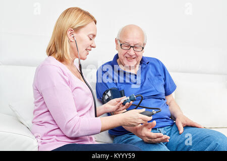 Junge Frau mit Blutdruck überwachen steuert den Blutdruck in einer älteren Stockfoto