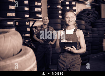 Lächelnden jungen Frau in Uniform stehen und schreiben Sie die Daten in auto Werkstatt Stockfoto