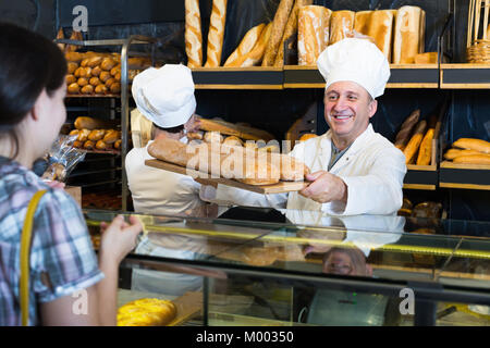 Junge Frau mit frischem Baguette unter anderem Brot vom Bäcker im Shop Stockfoto