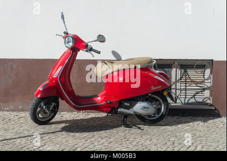 Leuchtend rote Vespa Motorroller auf einer gepflasterten Straße geparkt. Stockfoto