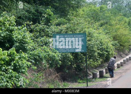 Mann zu Fuß vorbei an Schild mit Geschwindigkeitsbegrenzung und Mosi-Oa-Tunya Nationalpark Eintrag nach Victoria Falls Bridge, Livingstone; Sambia. Stockfoto