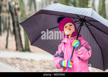 Wenig liebenswert kaukasische Mädchen mit rosa warme Jacke und Strickmütze wandern unter dem Dach in einem Stadtpark an kalter Tag. Stockfoto