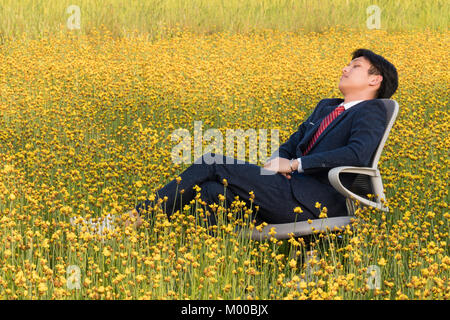 Asiatische Geschäftsmann liegt auf einem Stuhl in einem großen gelben Blume Bereich Stockfoto