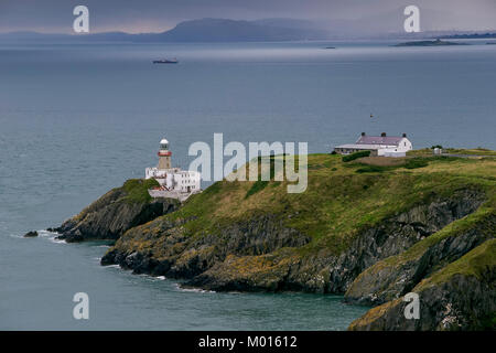 Ein Foto des Bailey Lighthouse in der Bucht von Dublin mit Dalkey Inseln über die Bucht und die Wicklow Mountains im Nebel darüber hinaus. Stockfoto