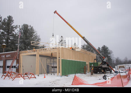 Ein LKW-montierte Kran Dachstühle auf ein Gebäude hinaus in einem Schneesturm in der Spekulant, NY, USA Stockfoto