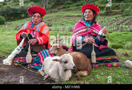 Frauen und Lamm. Peruanische Frauen Spinnen Garne. Die peruanischen Frauen in traditioneller Kleidung ein Garn weben, sitzen auf einer Wiese in der Nähe von Schafen Stockfoto