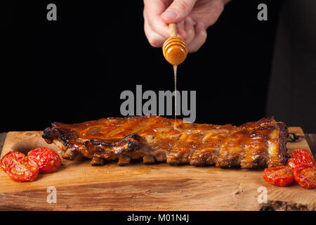 Cooking Pork Rib Koteletts mit Honig süßen Soße auf dunklem Hintergrund. Der Küchenchef gießt Honig Rippchen. Mit kopieren. Stockfoto