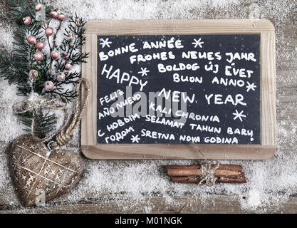 'Frohes neues Jahr' in verschiedenen Sprachen auf einer Schiefertafel mit Winter Dekorationen geschrieben Stockfoto