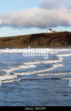 Blick auf ein weißes Haus auf den Klippen am Ende der Sandstrand, Porth Tywyn Mawr, Llanfwrog, Anglesey, über dem einströmenden Wasser Stockfoto