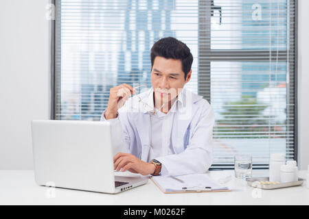 Männlicher Arzt am Schreibtisch in Doctor's Zimmer funktioniert Stockfoto