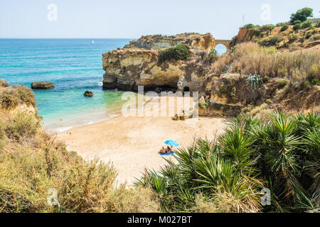 Student Strand oder Praia dos Estudantes in Lagos, Portugal. Ein paar Standortwahl am Strand unter einem blauen Sonnenschirm. Stockfoto