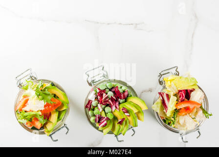 Frische Salate in Glas mit frischem Gemüse und gesunde Dressings, auf weissem Marmortisch, kopieren Raum Stockfoto