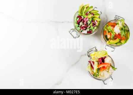 Frische Salate in Glas mit frischem Gemüse und gesunde Dressings, auf weissem Marmortisch, kopieren Raum Stockfoto