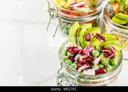 Frische Salate in Glas mit frischem Gemüse und gesunde Dressings, auf weissem Marmortisch, kopieren Raum Stockfoto