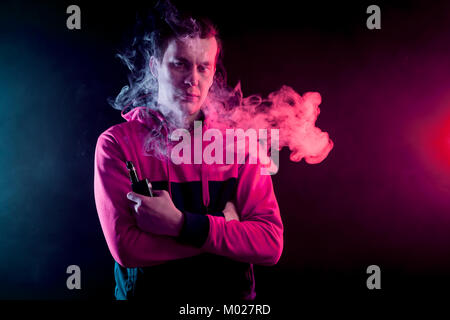 Portrait einer jungen gutaussehenden Mann mit vape und Ausatmen eine große Wolke von Rauch auf einem dunklen Hintergrund Stockfoto