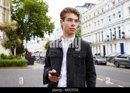 Junge Mann in Street holding Smartphone entfernt suchen Stockfoto