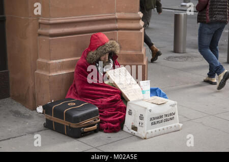 Obdachlosen Mann sitzt auf einem sehr kalten Winter Tag um Hilfe zu bitten, im Financial District, in Lower Manhattan, NYC gebündelt. Stockfoto