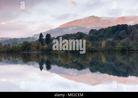 Ein ruhiger, noch morgen am Coniston Water im Lake District mit frühen Morgen Licht auf dem Hügel in Richtung der Alte Mann von Coniston. Stockfoto