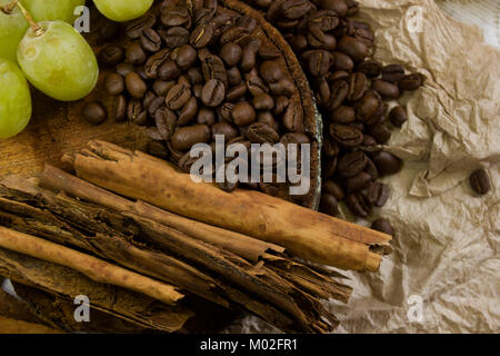 Blick von oben auf eine gemütliche Szene von Kaffeebohnen auf rustikalen, mit Holz, Stöcke von Zimt und Trauben Stockfoto