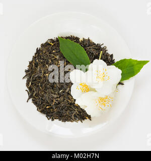 Jasmin trockener grüner Tee auf weißem Teller mit dekorierten frischen Blumen auf weißem Hintergrund. Draufsicht. Stockfoto