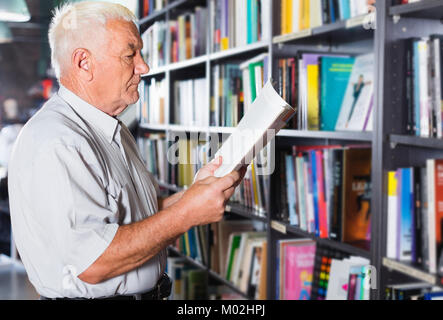 Mann 53-64 Jahre alt ist die Wahl Buch zum Lesen in der freien Zeit in der Buchhandlung. Stockfoto