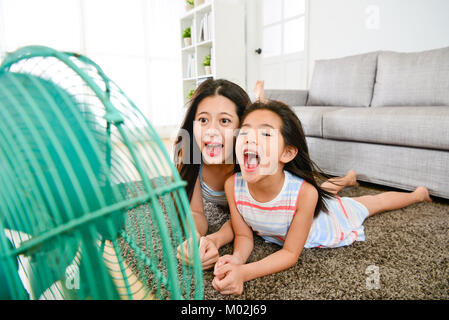 Heitere Schönheit kleines Mädchen mit Mutter zusammen spielen elektrischer Ventilator zu Hause, wenn Sie auf dem Boden liegend entspannen während der Sommersaison. Selektive f Stockfoto