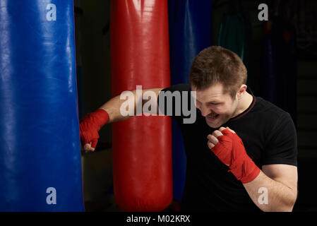 Starke kickboxer Mann stanzen Blue Sand Beutel auf gym Hintergrund Stockfoto