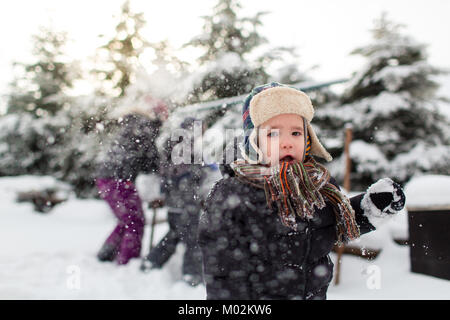 Vorderansicht eines kleinen Kindes mit offenen Mund und seine Familie in Schneeballschlacht im Hintergrund. Familie mit Schnee. Stockfoto