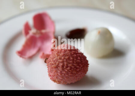 Geschälte und ungeschälte Lychee auf einer Platte Stockfoto