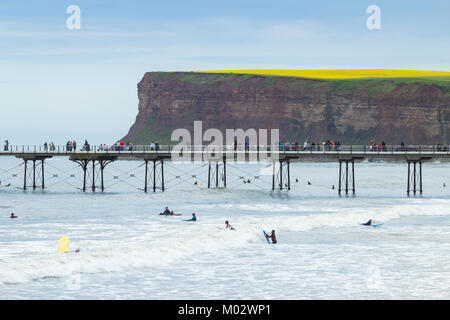 Surfer in der Nähe der viktorianischen Saltburn Pier mit Wanderern auf Klippe Wanderweg (der Cleveland Way) in der Entfernung. Durch das Meer, Yorkshire, England Saltburn. Großbritannien Stockfoto