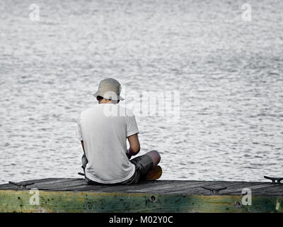 Südöstlichen TX USA - April 1, 2017 - Mann sitzt auf einem hölzernen Dock über das Wasser. Stockfoto