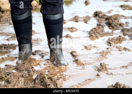 Eine Frau zu Fuß durch dicke Schlamm auf Sodden nassen Boden. Sie ist das Tragen von Gummistiefeln. Der Schlamm Knöchel tief in den Plätzen machen es schwierig zu gehen Stockfoto