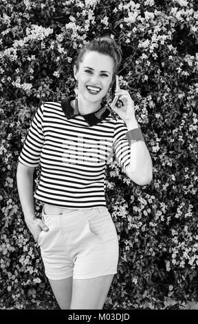 Bunte Frische. glückliche junge Frau in gelb gestreifte Hosen und Hemd in der Nähe der bunten magenta Blumen Bett mit einem Mobiltelefon Stockfoto