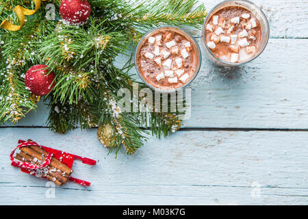 Zwei Gläser Kakao mit Marshmallows und Weihnachtsbaum mit Spielzeug auf weißem Holz- Hintergrund. Stockfoto