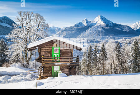 Panoramablick auf die wunderschöne Winterlandschaft Berglandschaft der Alpen mit traditionellen Mountain Chalet an einem kalten sonnigen Tag mit blauem Himmel und Clou Stockfoto